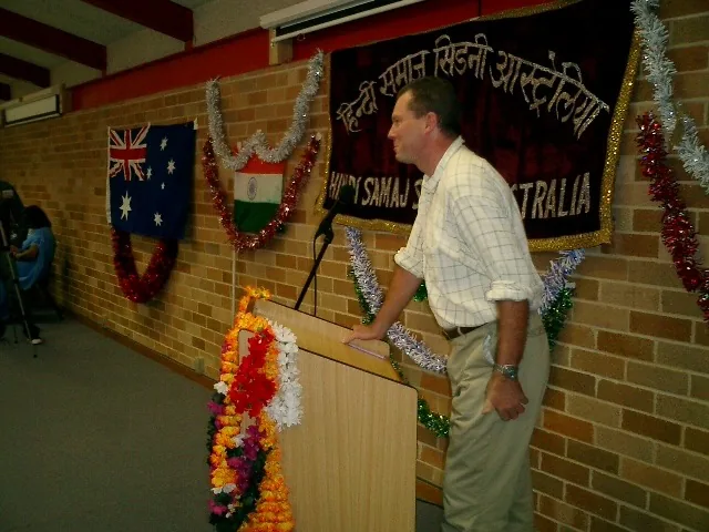 A guest addressing the inauguration from a lectern beside the Hindi Samaaj banner